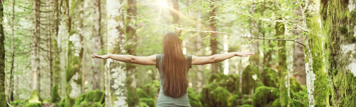 Eine Frau breitet ihre Arme aus und genießt die Sonne und den Wald